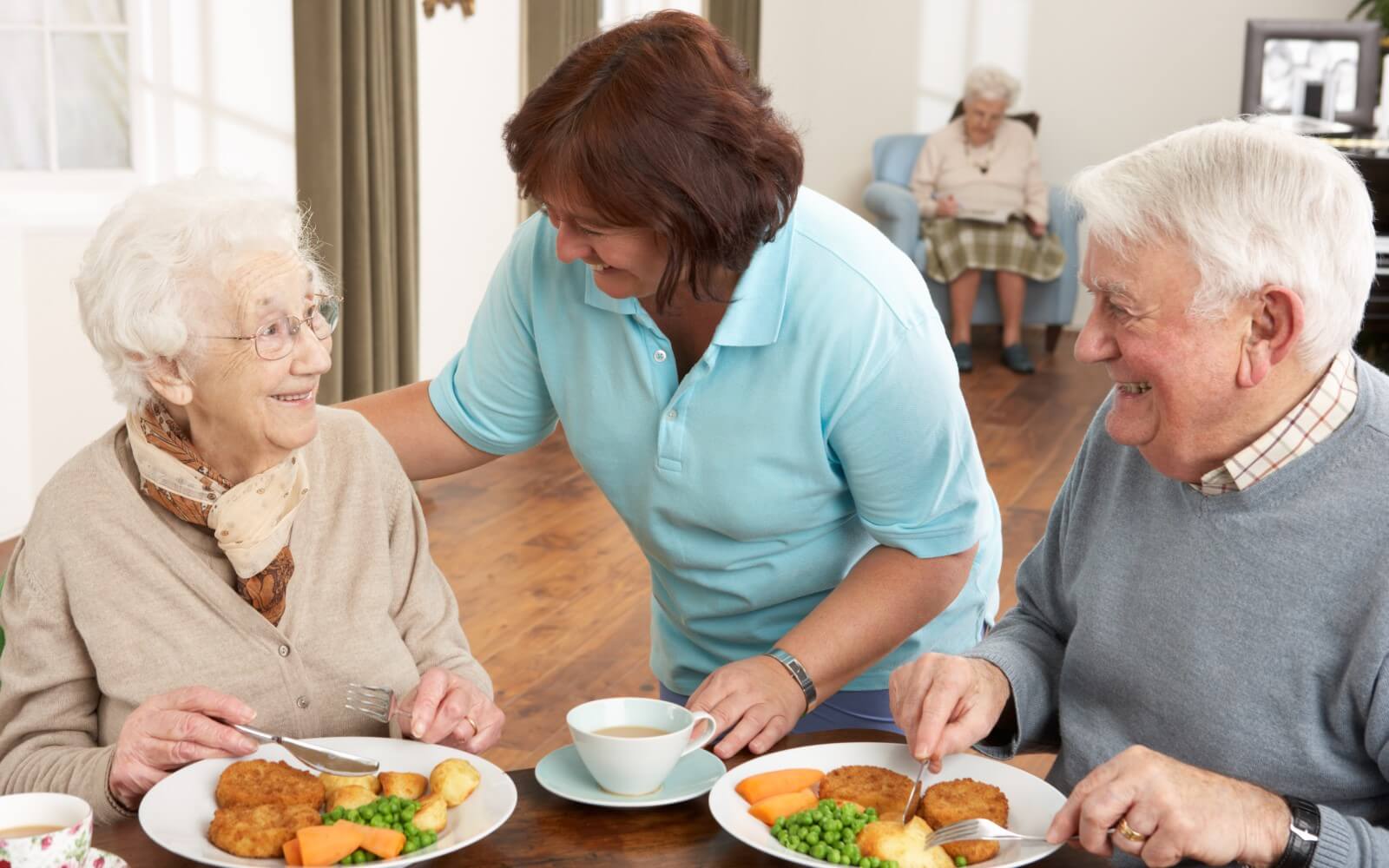 Hauswirtschaftskraft serviert alten Menschen das Mittagessen in der Altenpflegeeinrichtung.