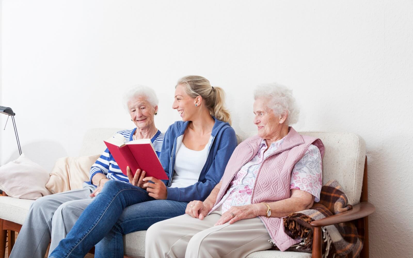 Pflegekraft liest Märchen aus einem Buch vor, 2 ältere Frauen hören ihr zu.