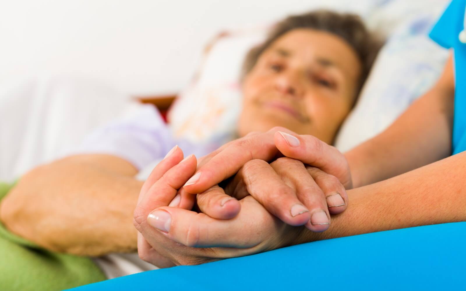 Pflegefachkraft hält die Hände einer dementen, alten Frau